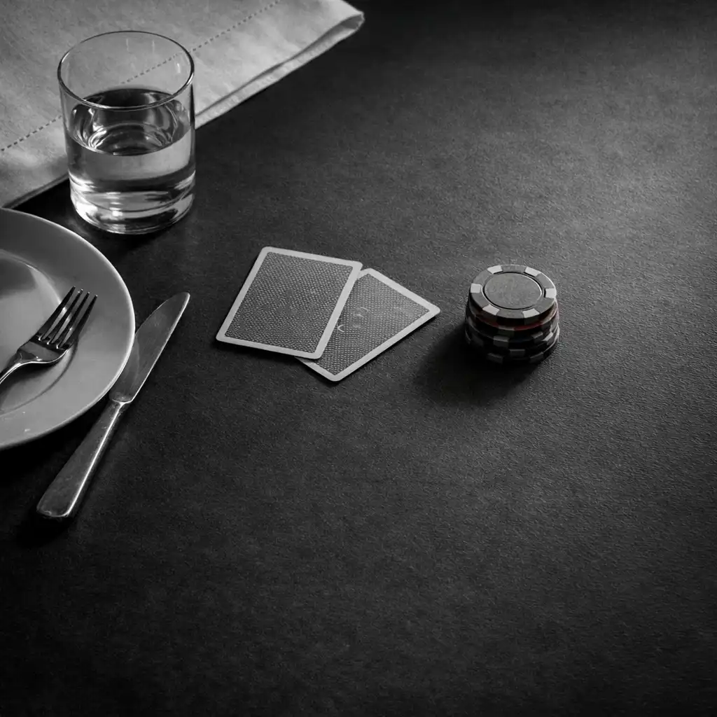 White linen, a water glass, place setting, face-down cards and plain chips on a dark table